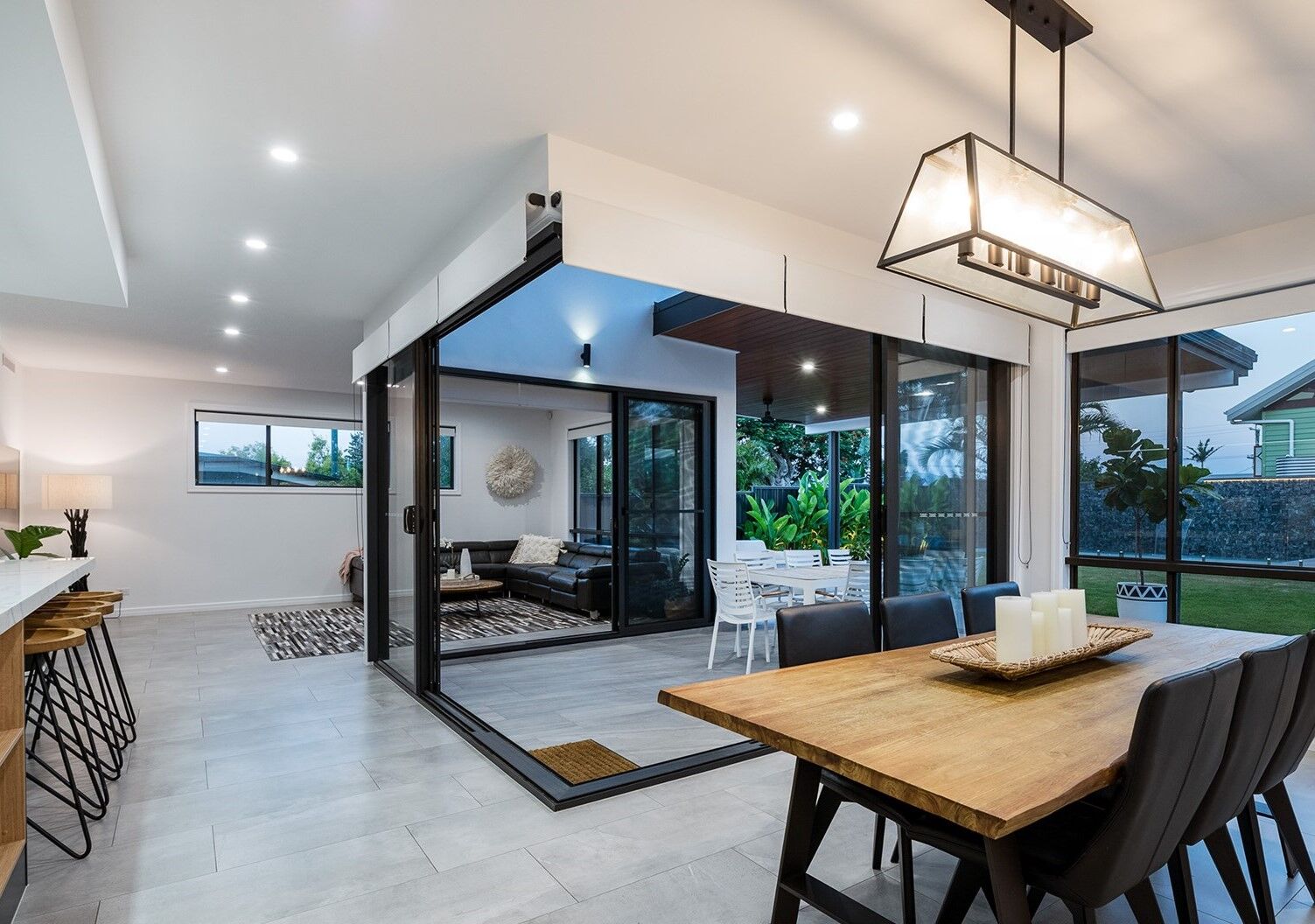 A modern dining room with table, bar with stools, semi-outdoor dining and blinds in windows