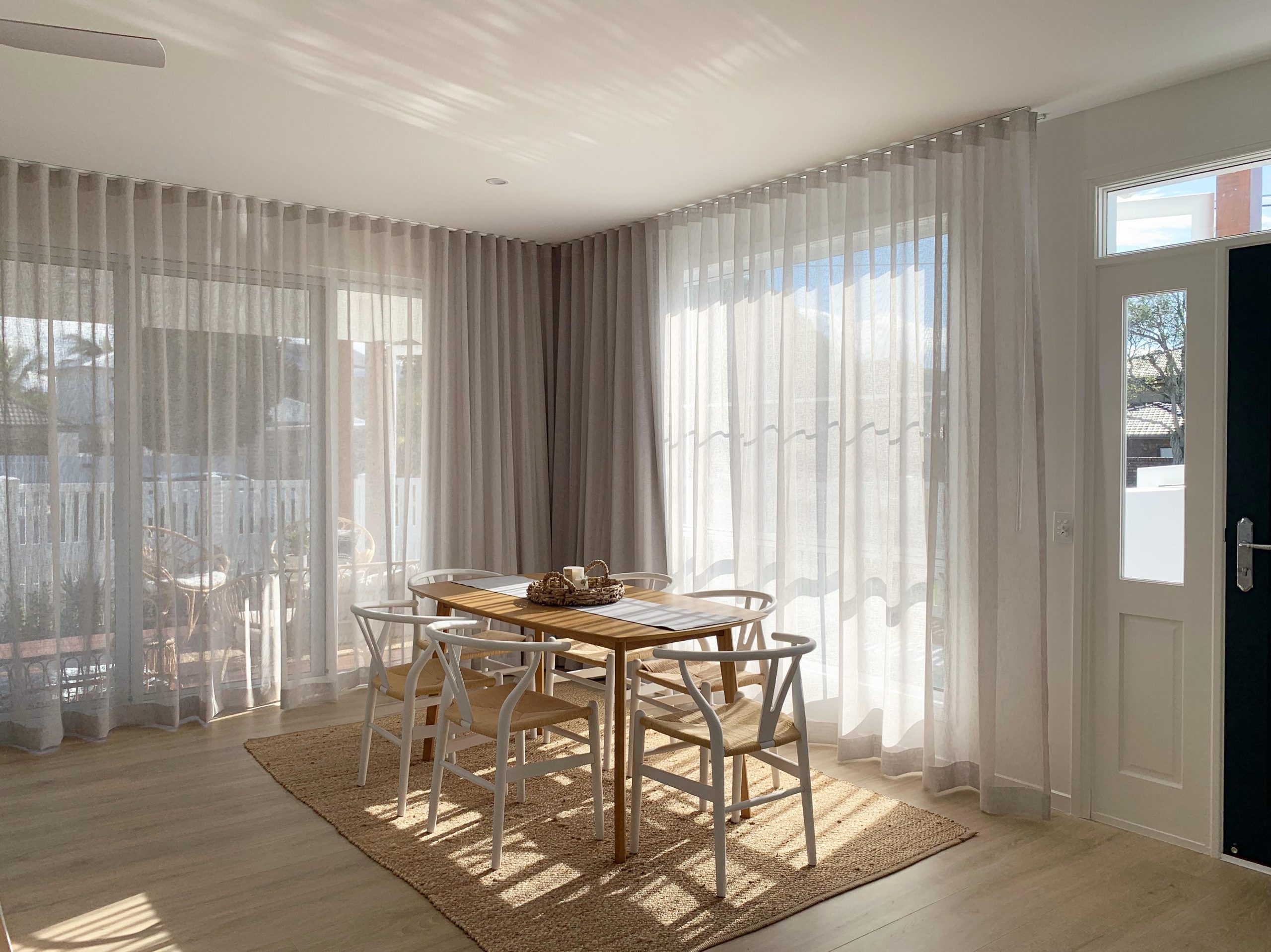 A modern dining room on a sunny day with small dining table surrounded by chairs and with Blindo curtains in the windows.