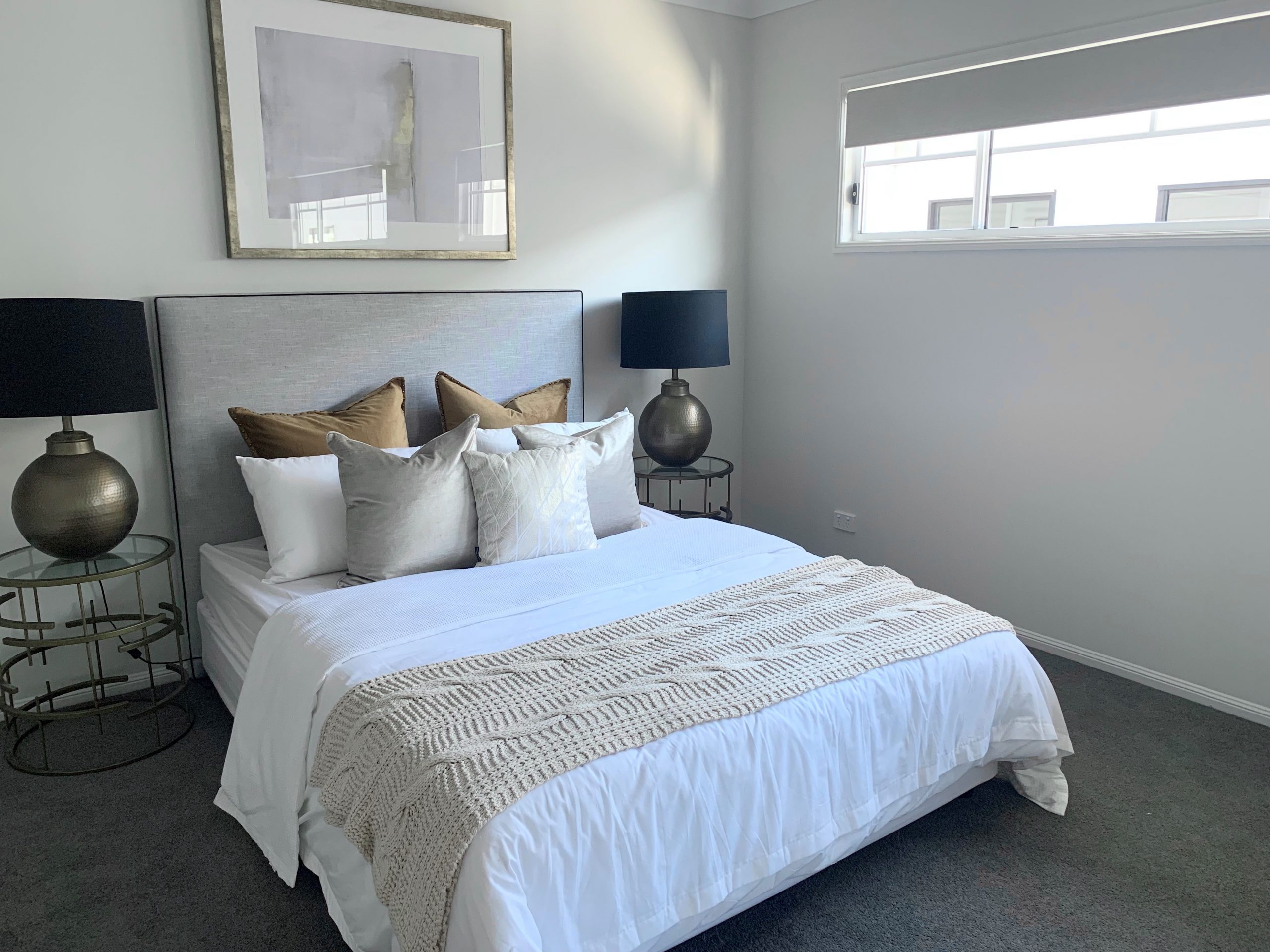 A modern bedroom wiht a large bed, stacked with pillows and blinds purchased online in the windows,