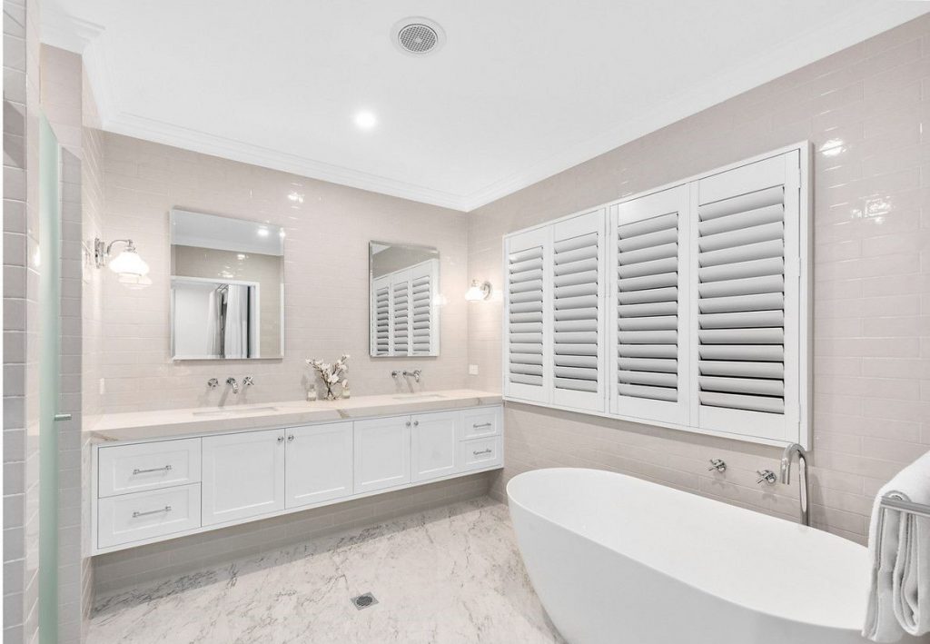 A bathroom with a freestanding bath and white shutters | Featured image for the blog How to Clean Shutters and Get Them Looking New from Blindo.